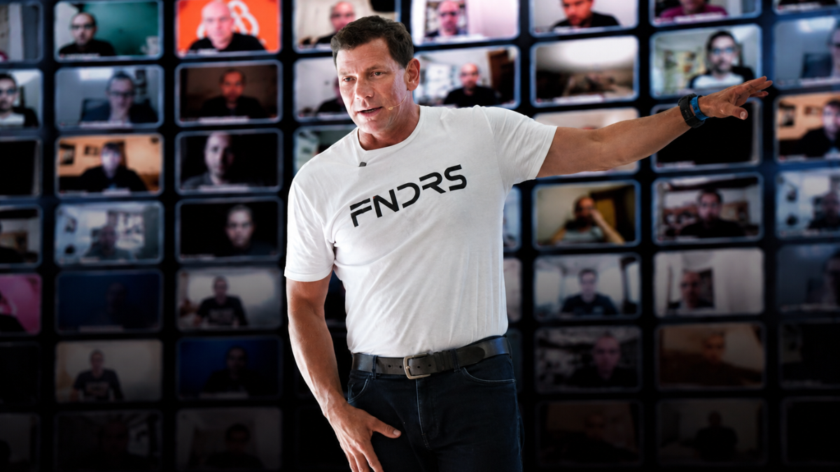 Troy on stage in a FNDRS shirt, a wall of founders on video behind him